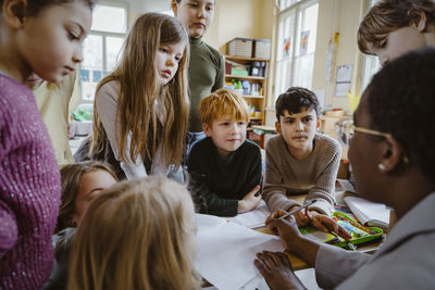 Boys and girls looking at teacher explaining in classroom at elementary school