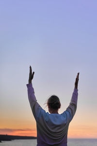 Rear view of man with arms raised against sky during sunset