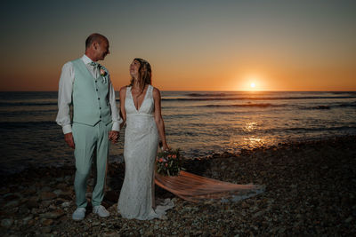 Bride and groom standing on beach during sunset