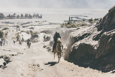 People riding horses on land by rock formation