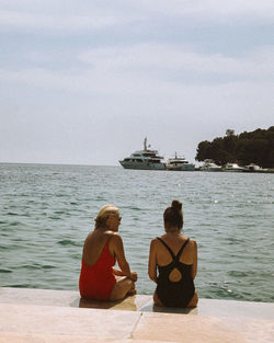 Rear view of women sitting on shore against sea