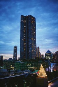 Illuminated skyscrapers against cloudy sky at dusk