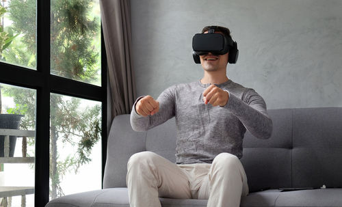 Smiling man using virtual reality simulator while sitting on sofa at home