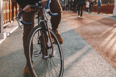 Low section of cyclist riding bicycle on bridge in city during sunset