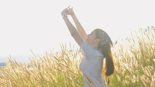 Woman with arms raised standing on field against sky