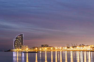 Illuminated buildings by river against sky at night