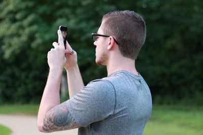 Side view of young man photographing with mobile phone at park