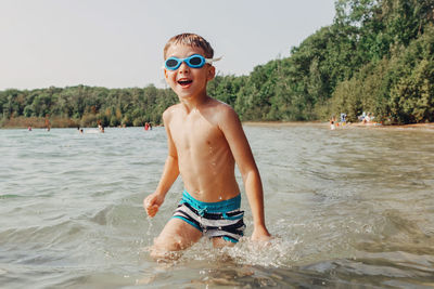 Portrait of cheerful boy walking in sea against sky