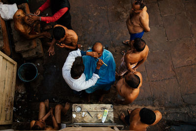 Varanasi, india - february, 2018: from above of barbers shaving locals on city street and bare chested men waiting in queue