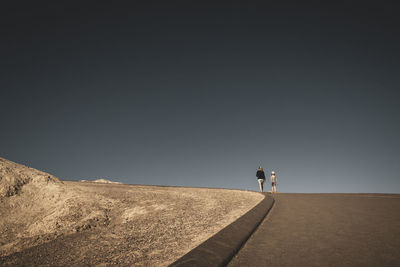 Rear view of mother walking with daughter against sky on road