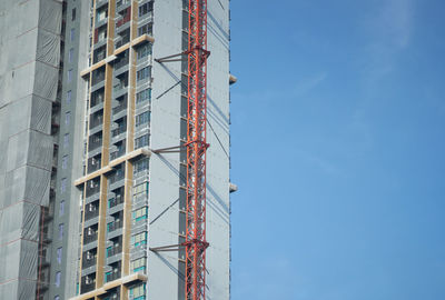 Low angle view of crane and buildings against blue sky