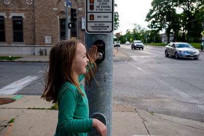 Young girl pushing crosswalk button at intersection