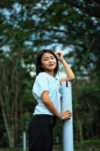 Portrait of smiling young woman standing against trees