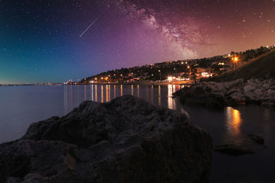 Sea by illuminated city against sky at night