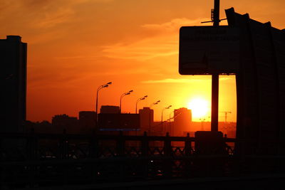 Silhouette city street against orange sky