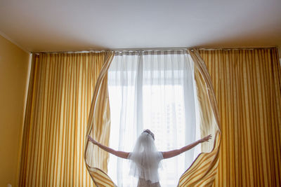 Rear view of woman standing against curtain