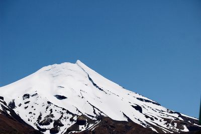 Low angle view of snowcapped mountain against clear blue sky