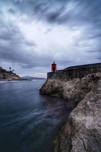 Lighthouse on rock by sea against sky