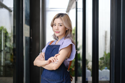 Portrait of young woman standing against window