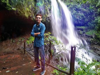 Full length of young man standing against waterfall in forest