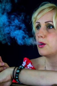 Close-up of woman smoking against black background