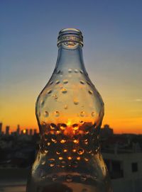 Close-up of glass bottle against sky during sunset