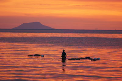 Silhouette of fisherman in sea during sunset