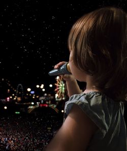 Rear view of boy holding mobile phone at night