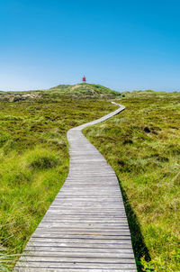 Boardwalk leading towards landscape against clear sky