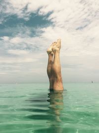 Upside down image of man in sea against cloudy sky