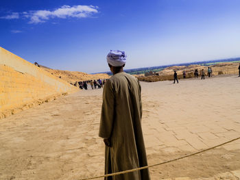 Rear view of man standing on desert against blue sky