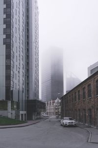 Cars on road by buildings against sky in city