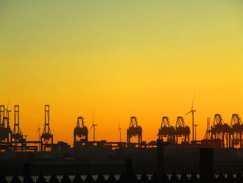 Silhouette cranes on pier against sky during sunset