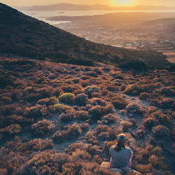 Rear view of woman sitting on mountain during sunset