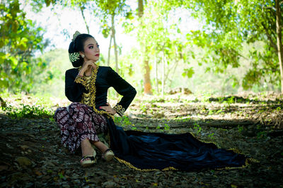 Portrait of young woman sitting against trees