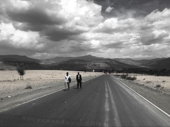 Men walking on road against cloudy sky