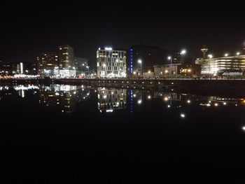 Illuminated buildings by river against clear sky at night