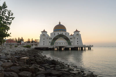 Mosque over sea against sky during sunset