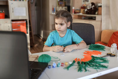 Girl making decoration while looking at laptop on table at home
