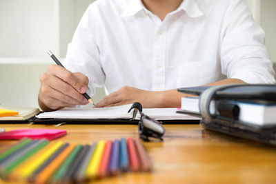 Midsection of man holding paper while sitting on table