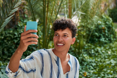 A young man with afro hair is doing a self-portrait in a park