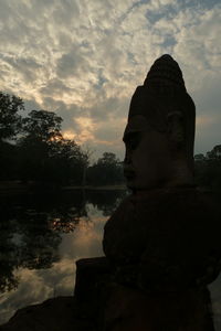 Statue by lake against sky during sunset