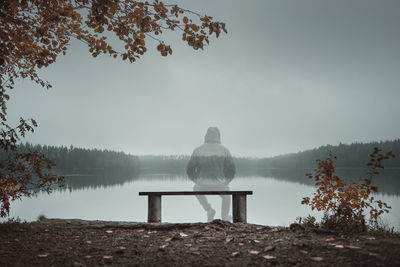 Lonely man sitting on bench at lake against sky