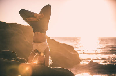 Woman standing on rock at sea shore against sky during sunset