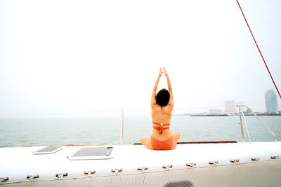 Rear view of woman sitting in sea against sky