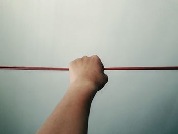 Cropped hand holding clothesline against wall