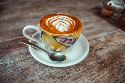 Cup of coffee with cream pattern, mug with pattern, spoon on wooden table. morning cappuccino.