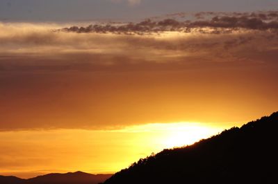 Scenic view of dramatic sky over silhouette landscape during sunset