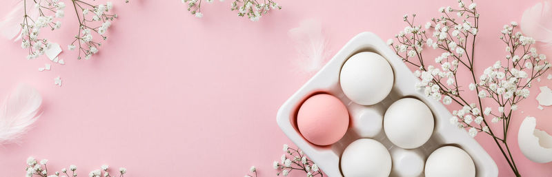 High angle view of eggs in tray by flowers on pink background