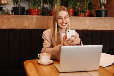 A business woman with glasses works and studies online using a mobile phone and technology in a cafe